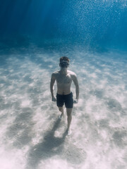 Sporty man freediver stay on sand bottom underwater in sea.