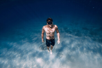 Fototapeta na wymiar Freediver in red swimsuit with fins posing underwater over sand in ocean.