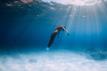 Woman freediver in swimsuit with fins glides underwater over sand in ocean.