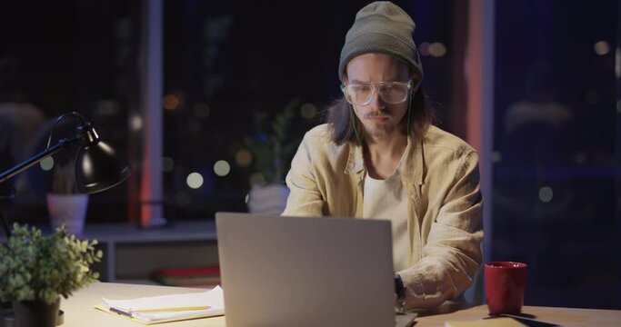 Young unweel caucasian hipster guy finishing project having computer virus problems internet connection getting worried while working at night office.