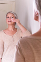 A elderly Caucasian women with short gray hair in casual clothes cares for the skin of the face.