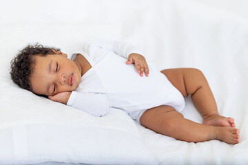 African-American little baby sleeps on a white bed at home with her hand folded under her cheek