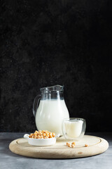 Alternative vegan milk of chickpeas in a glass jug on a wooden round board against a dark background