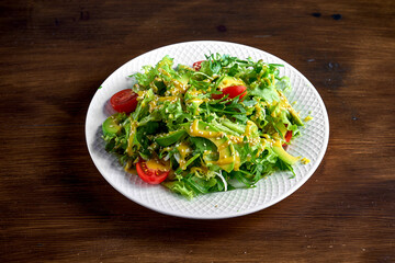 Healthy and dietary salad mix with avocado, sesame seeds, yellow dressing and cherry tomatoes, served in a white plate on a wooden background