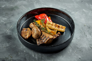 Appetizing grilled vegetables served in a black plate on a gray background. Vegetable kebab