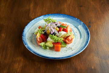 Classic Greek salad with tomatoes, cucumbers, red onions, feta cheese and olives, served in a blue plate on a wooden background.