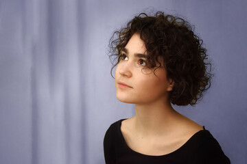 Portrait of a young girl with a curly hairstyle on a purple background.