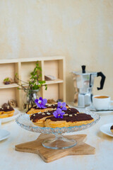 Dessert, choux pastry sweets with vanilla custard, covered with chocolate glaze, on a glass stand on a light concrete background. French cuisine.