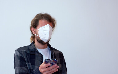 A Spanish young bearded male wearing a protective facemask incorrectly and looking at the phone