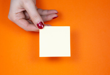 Blank yellow To Do List Sticker in woman hand. Close up of reminder note paper on the orange...