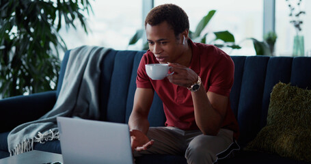 African american student with earphones staying home drinking coffee watching videochat online...
