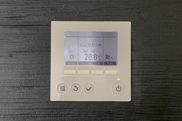 Air conditioning control panel. Digital thermostat on black wooden wall. Thermostat digital programmable