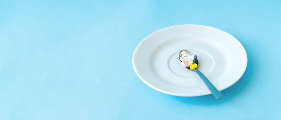 Colored pills in spoon. White plate on a blue background. Medicine for the patient or diet pills....