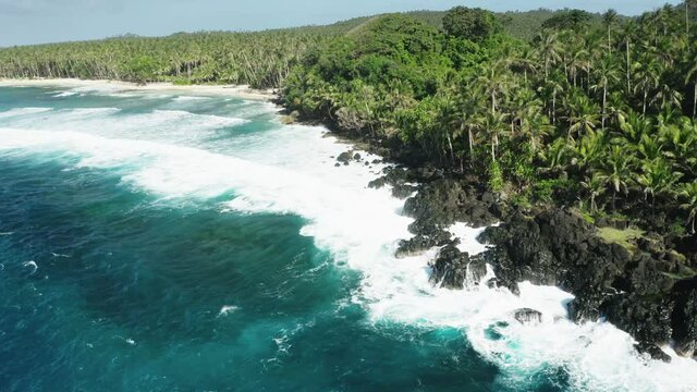 Turquoise water and white waves crushing over rocky coast, palm trees above. North part of Siargao Island, Philippines. Aerial view, 4h