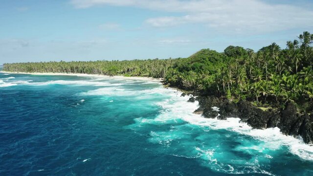 Calm  view of ocean waves crushing over rocky shore. Turquoise water, rocks and palm trees. Tropical coast, siargao island, Philippines. Aerial 4k
