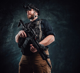 Fototapeta premium Soldier with helmet and vest stays holding a rifle in dark background