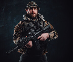 Fototapeta premium Serious guy in camouflage costume holding a rifle in dark background