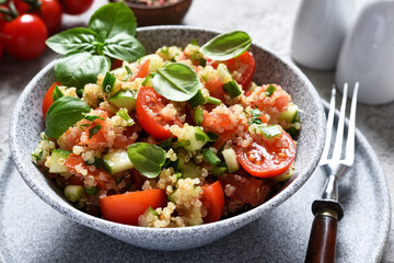 Light salad with tomatoes, cucumber and quinoa with olive oil and basil on a concrete background.