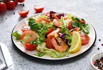 Mix salad with tomatoes and grilled shrimps with sauce and clematis on the kitchen table. Concrete food background.