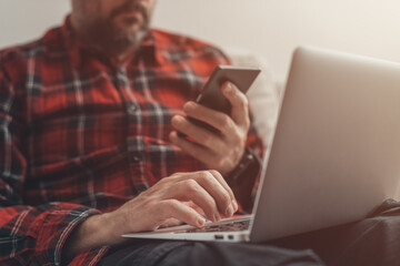Casual male working at home on laptop computer and mobile smart phone
