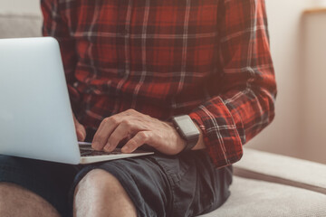 Casual man working from home on laptop computer while sitting at living room sofa