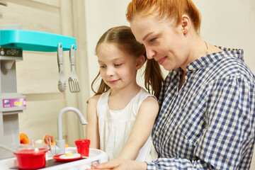 a caring mother plays with her daughter, teaches her the profession of a cook. the girl is very interested in how to cook properly.