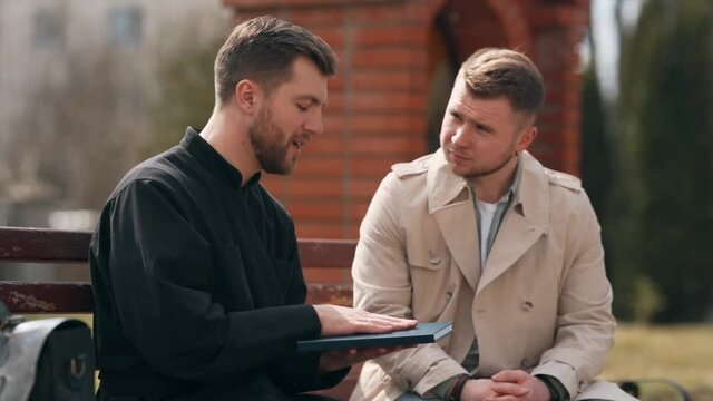 The priest talks to a young man sitting on a bench