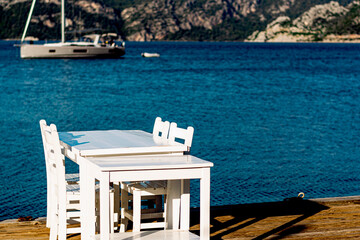 White tables of seaside cafe, or restaurant , sea, hills on background, yachting tourism food items, sailing boat on anchor
