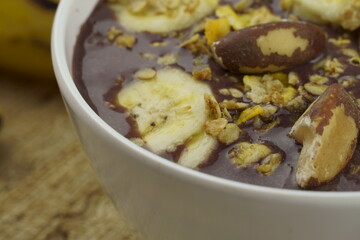 Brazilian açai in a white bowl with banana, granola and chestnuts. 