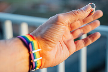 close-up view of a man's hand showing a ring with an LGBT rainbow wristband.