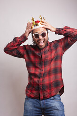 young Hispanic man with beard in his 30s celebrating wearing a king's crown and sunglasses, holding his head in his hands and smiling