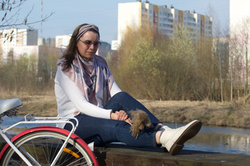 Naklejka premium Girl on a bike ride walk in the spring park. Sits on a park bench. There is a bicycle nearby.