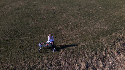 Girl on a bike ride walk in the spring park. Stands on the lawn in the park. She is holding a bicycle. Aerial photography taken with a drone.