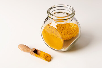 Curry spice powder in glass jar and wooden spoon on white background.