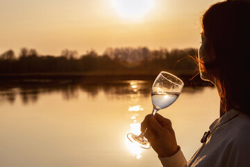 Woman with a glass looks at the sunset .