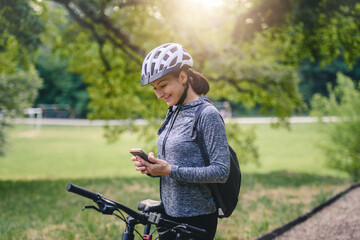 Smiling woman  cyclist in the public park using a smart phone