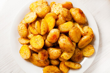 Baked appetizing crispy potato on white plate on the table. Top view. Close-up.