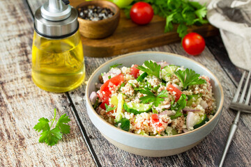 Food dieting concept, tuna salad. Couscous salad with conserved tuna, tomatoes, cucumbers and purple onions on rustic wooden table.