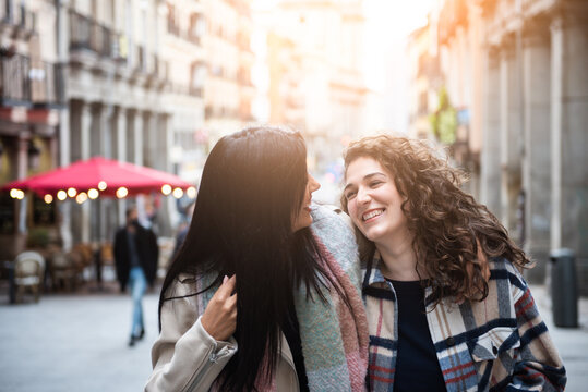 two girls walking, happy and laughing in the city. A couple of girls walk together. Women looking at each other and smiling.