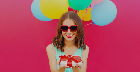 Portrait of happy young woman looking at gift box and colorful balloons on a pink background