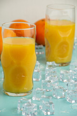 View of two glasses with orange juice, on blue table with ice and oranges, selective focus, vertical
