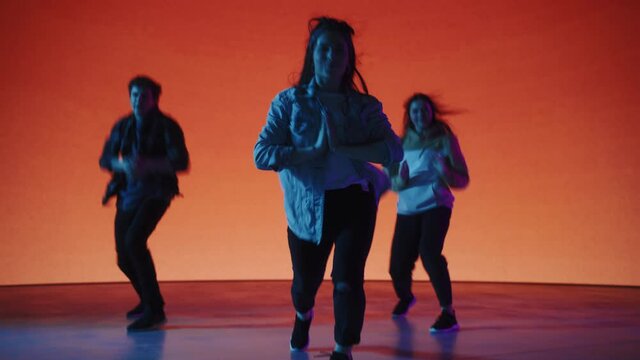 Diverse Group of Three Stylish Professional Dancers Performing a Hip Hop Dance Routine in Front of Big Led Wall Screen with Solid Orange Background During a Virtual Production in Studio Environment