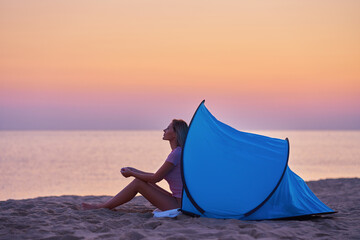 Silhouette of young woman in front of a tent at the beach at sunrise