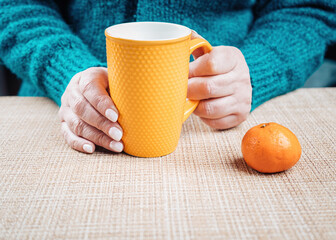 Woman sitting at the table and holding a yellow cup of tea in her hands