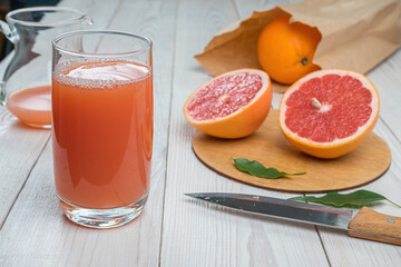 Fototapeta na wymiar Grapefruit juice in a glass on a wooden table, fresh cut oranges in the background