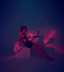 Modern girl with laptop, tablet computer. Free creativity. Young blogger in Home office. Colored Neon light