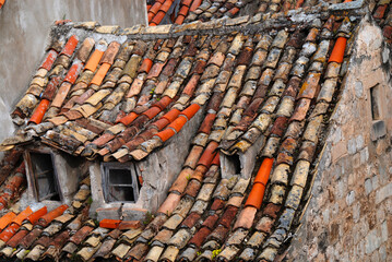 steep roof of ancient house with very old tiles and two windows