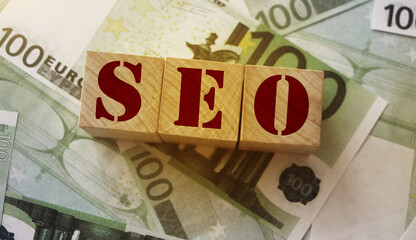 SEO - wooden blocks with letters, search engine optimization SEO concept, top view on 100 euro...