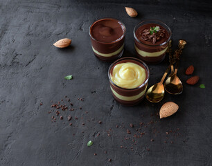 Dessert glass. Glasses of vanilla and chocolate vegan pudding with almonds and spoons on a dark background with space for text. Top view