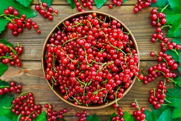 Ripe red currant berries in a bowl and around a bowl on a rustic wooden background. Red currant on brown wooden table
